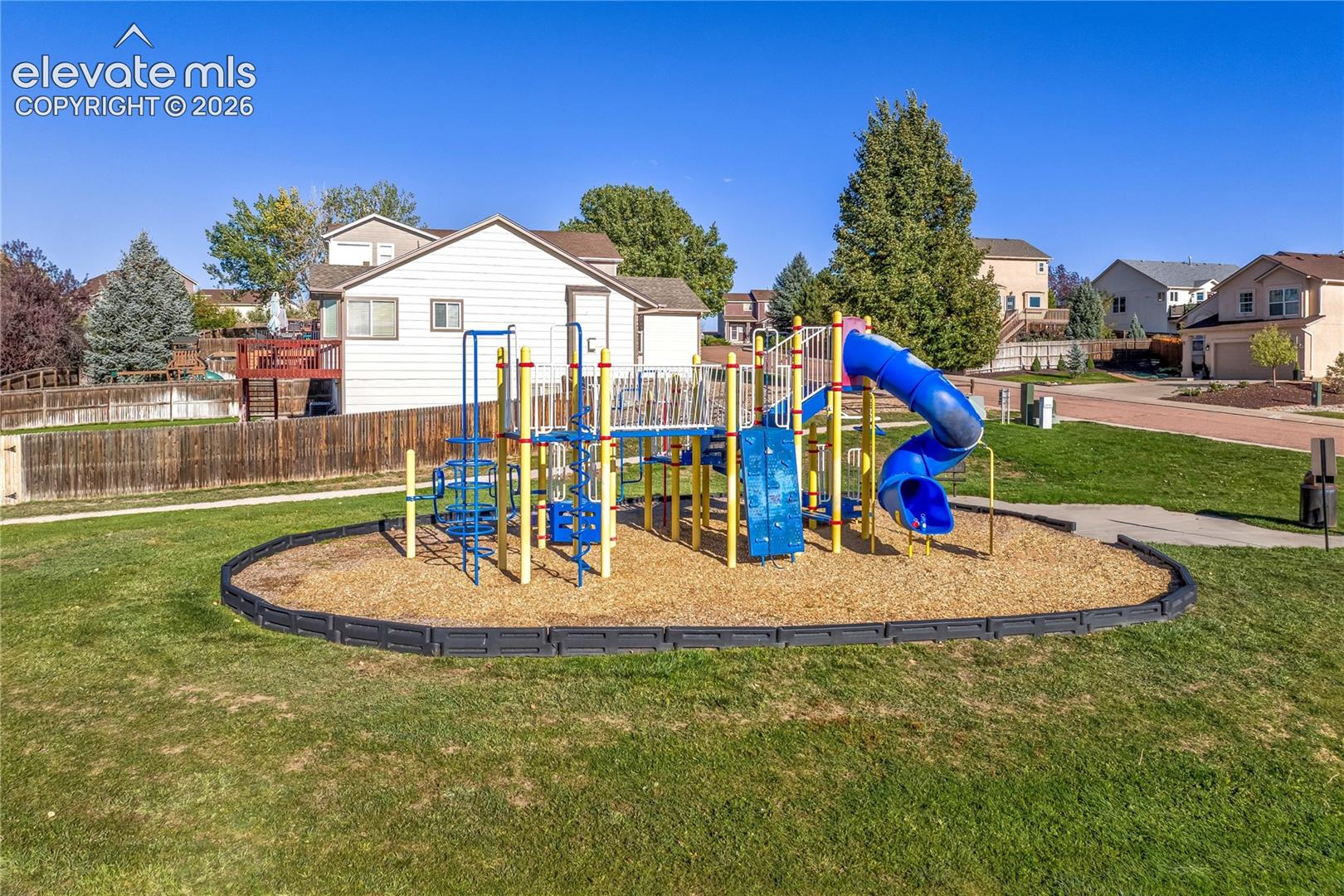 A colorful neighborhood playground features climbing structures, slides + surrounding grassy areas, offering a convenient outdoor recreation destination.