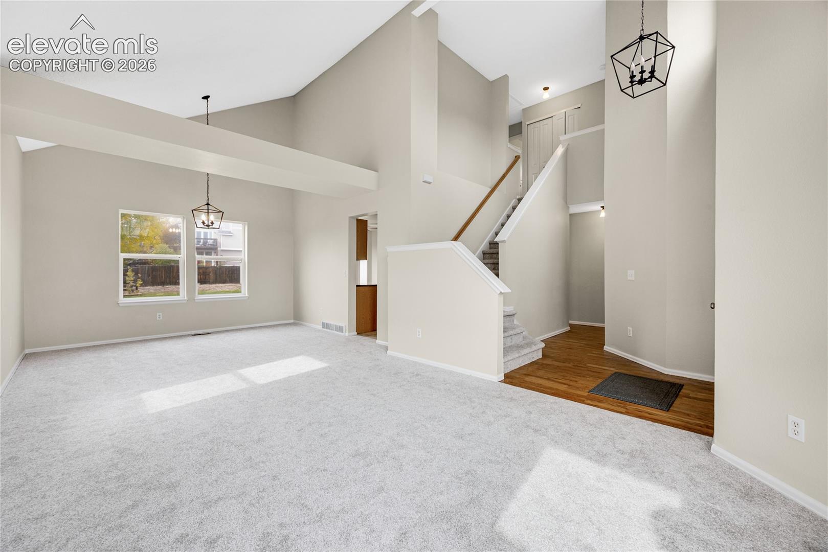 Vaulted ceilings with exposed beams, wood-finish flooring, carpeted staircase with wood handrail, and geometric pendant lighting