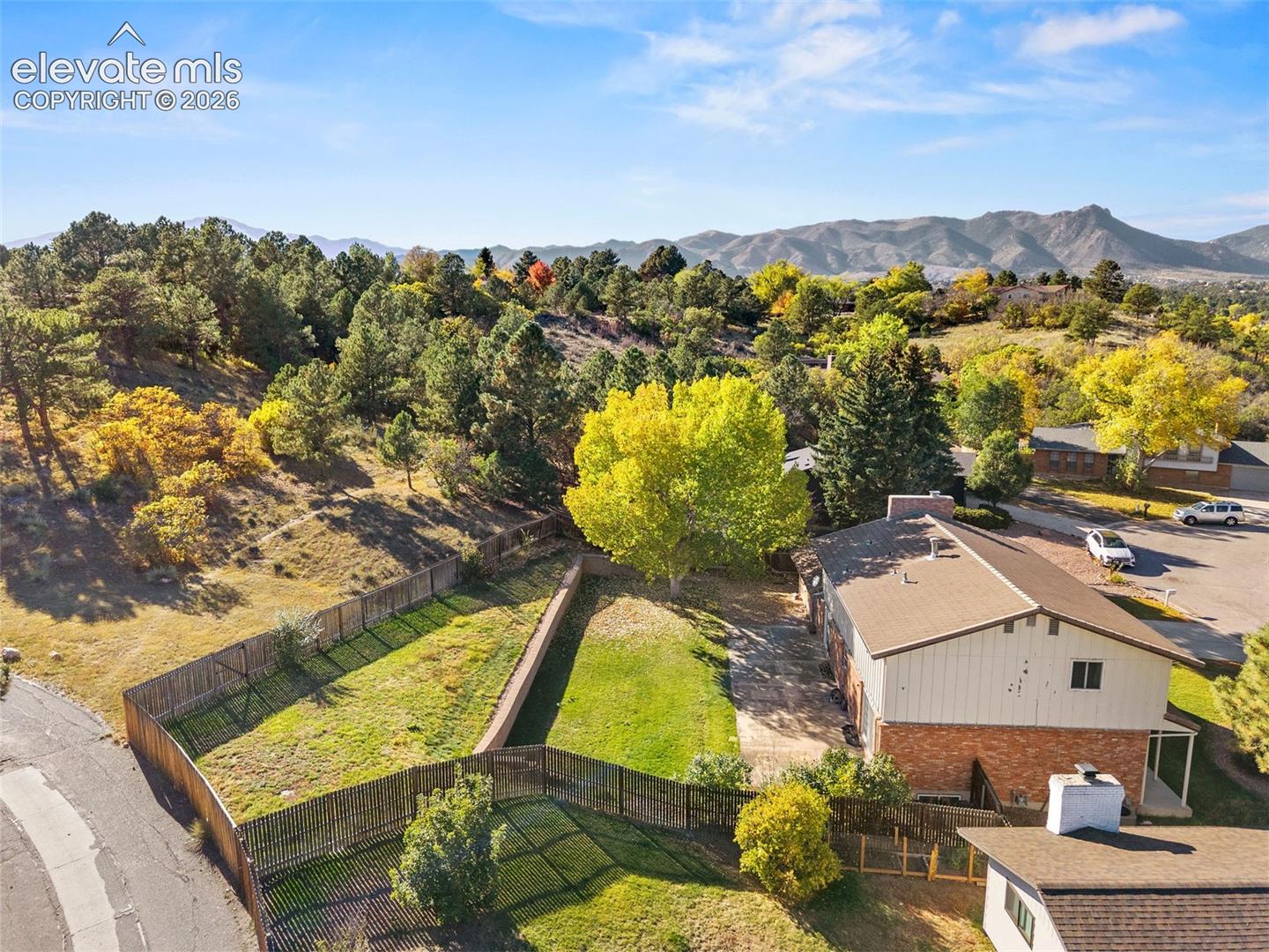 Property lot featuring expansive terrain, mature trees, mountain backdrop, brick and vertical siding exterior, and wood-style fencing
