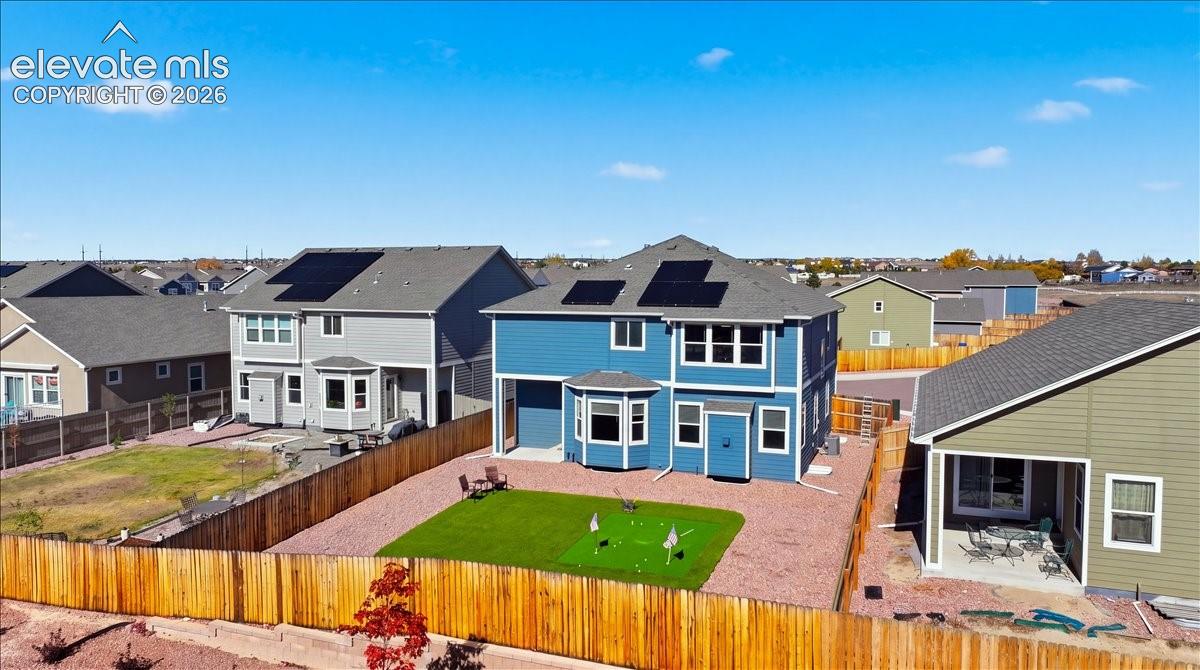 Two-story blue exterior siding with a shingled roof, roof-mounted solar panels, fenced backyard, and built-in artificial turf putting green