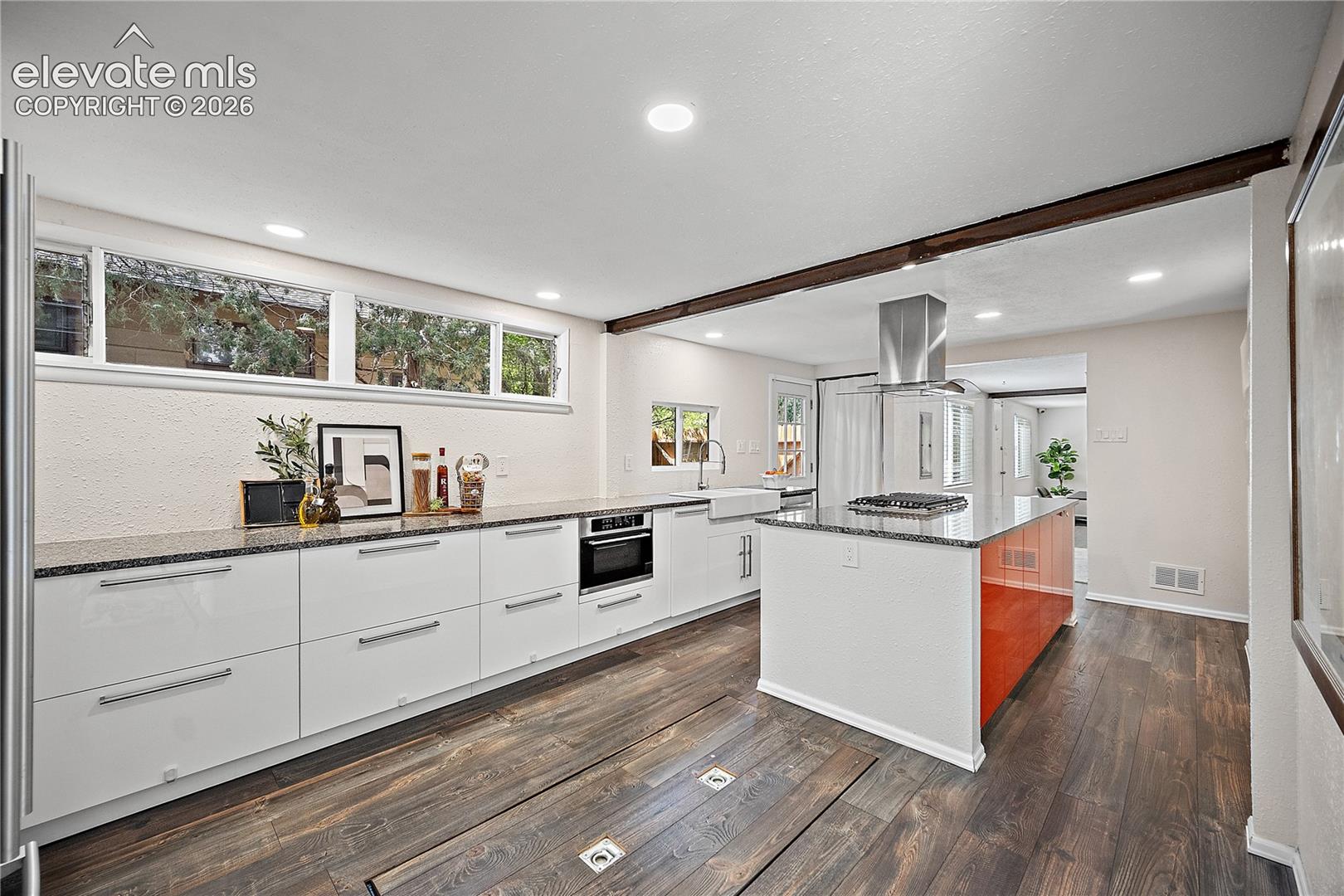 Modern kitchen featuring dark wood-finish flooring, white flat-panel cabinetry with long pulls, and a central island with a contrasting orange panel