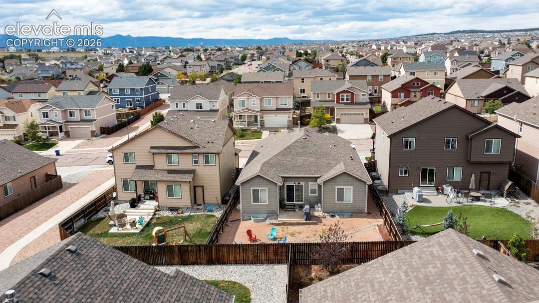 Aerial perspective of residential neighborhood featuring multi-story dwellings, fenced backyards, mountain backdrop, and composite shingle roofing
