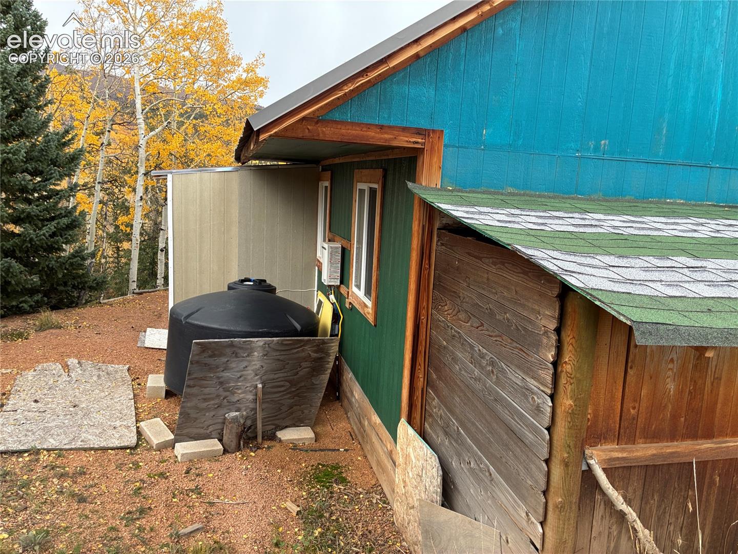 Exterior profile featuring multi-tonal vertical wood siding, green asphalt shingle roofing, and an attached storage structure