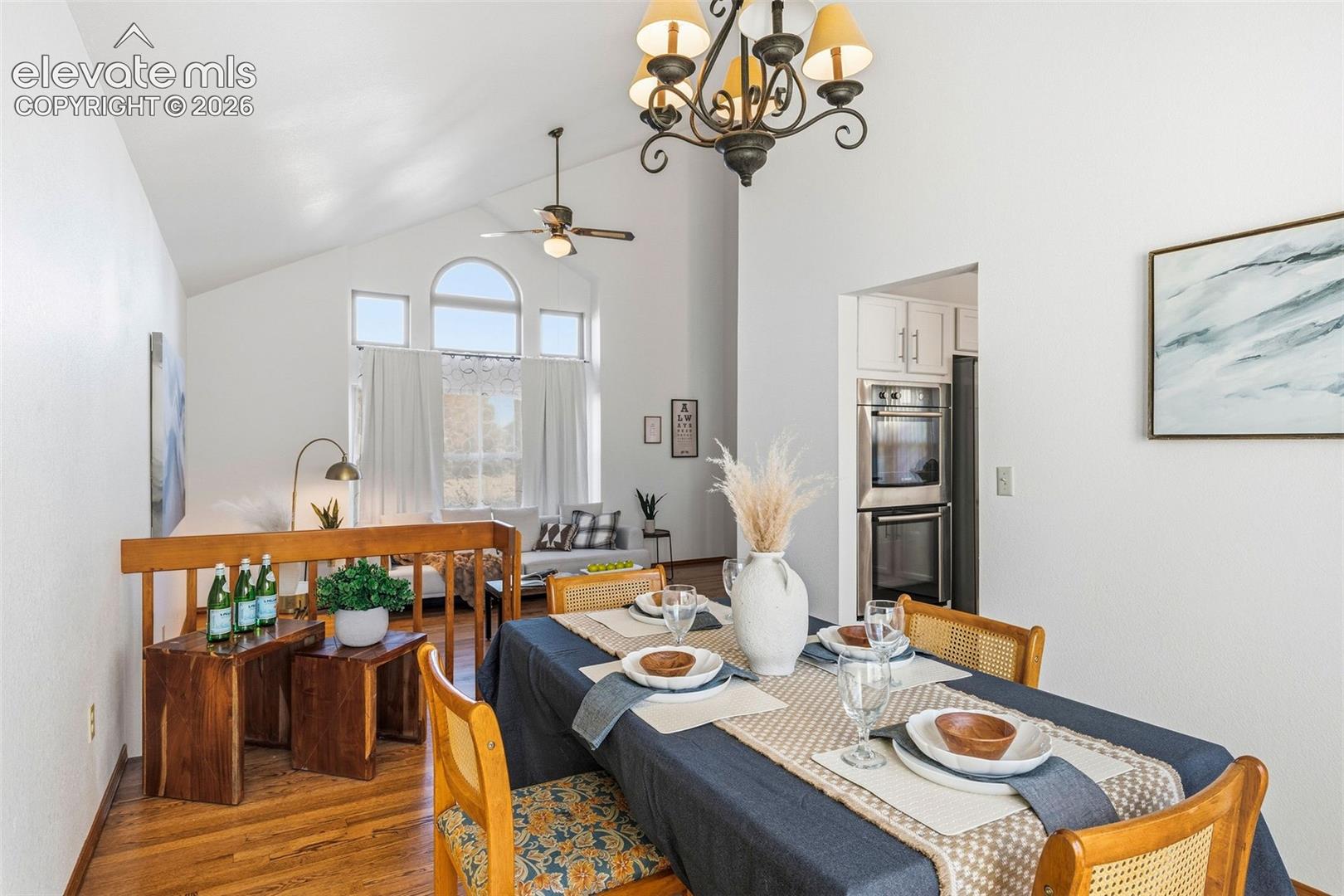 Vaulted ceilings, expansive arched windows, wood-finish flooring, ornate iron chandelier, and built-in stainless steel double wall ovens