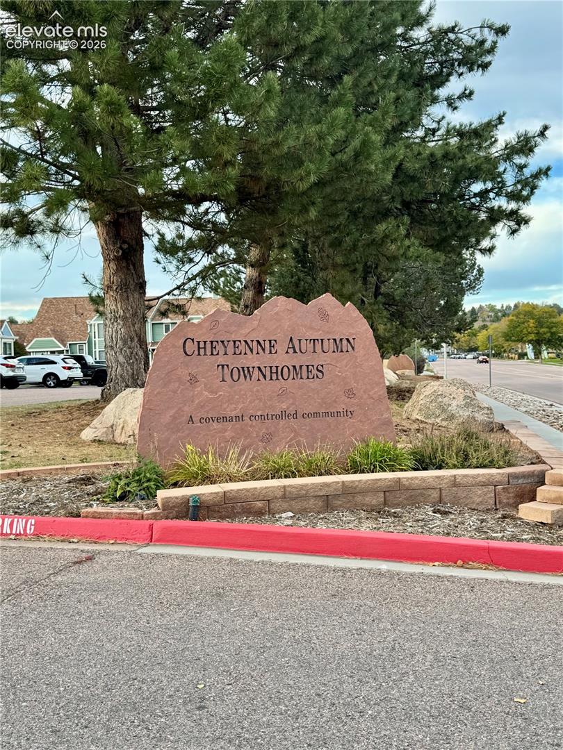 Community entrance featuring natural stone landscaping, mature evergreen trees, and a decorative rock monument