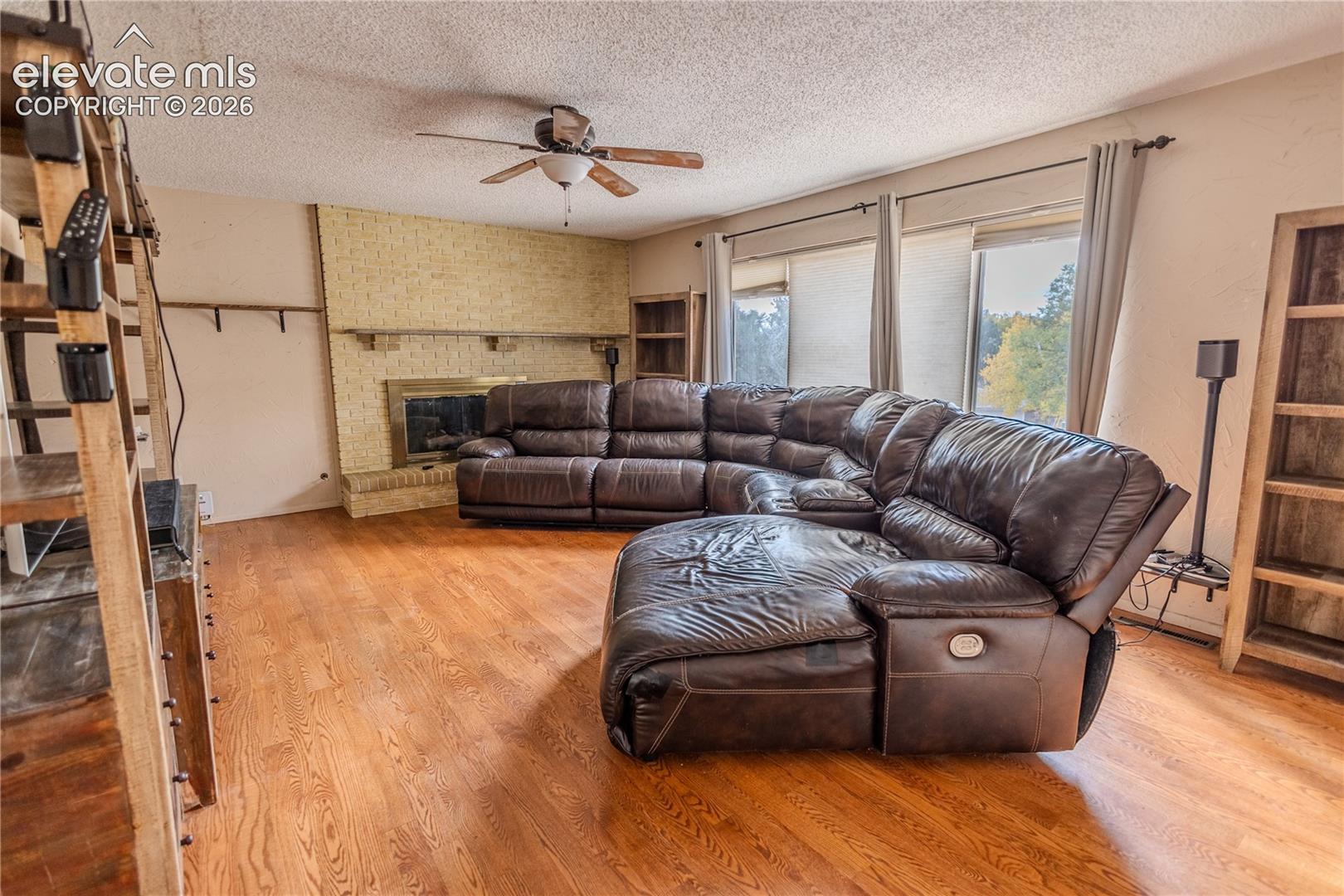 Living space featuring wood-finish flooring, a masonry fireplace with a built-in mantel, and a ceiling fan