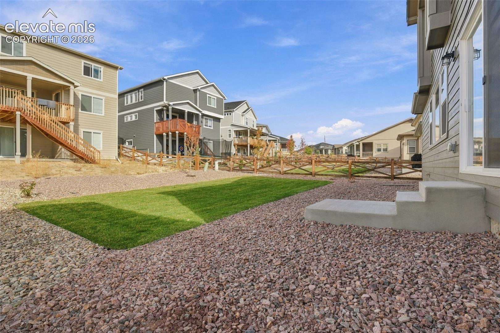 Backyard featuring a manicured lawn, decorative rock landscaping, concrete steps, and a wooden cross-buck fence