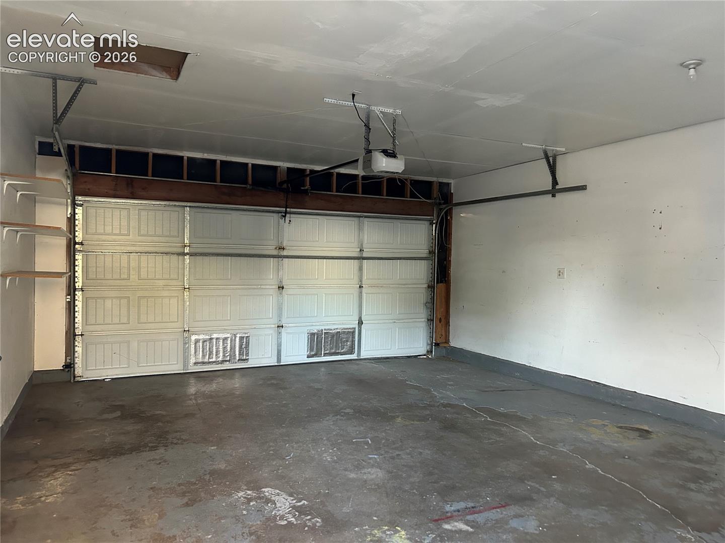 Multi-car garage featuring a sectional metal door, automated garage door opener, concrete flooring, and built-in wall shelving