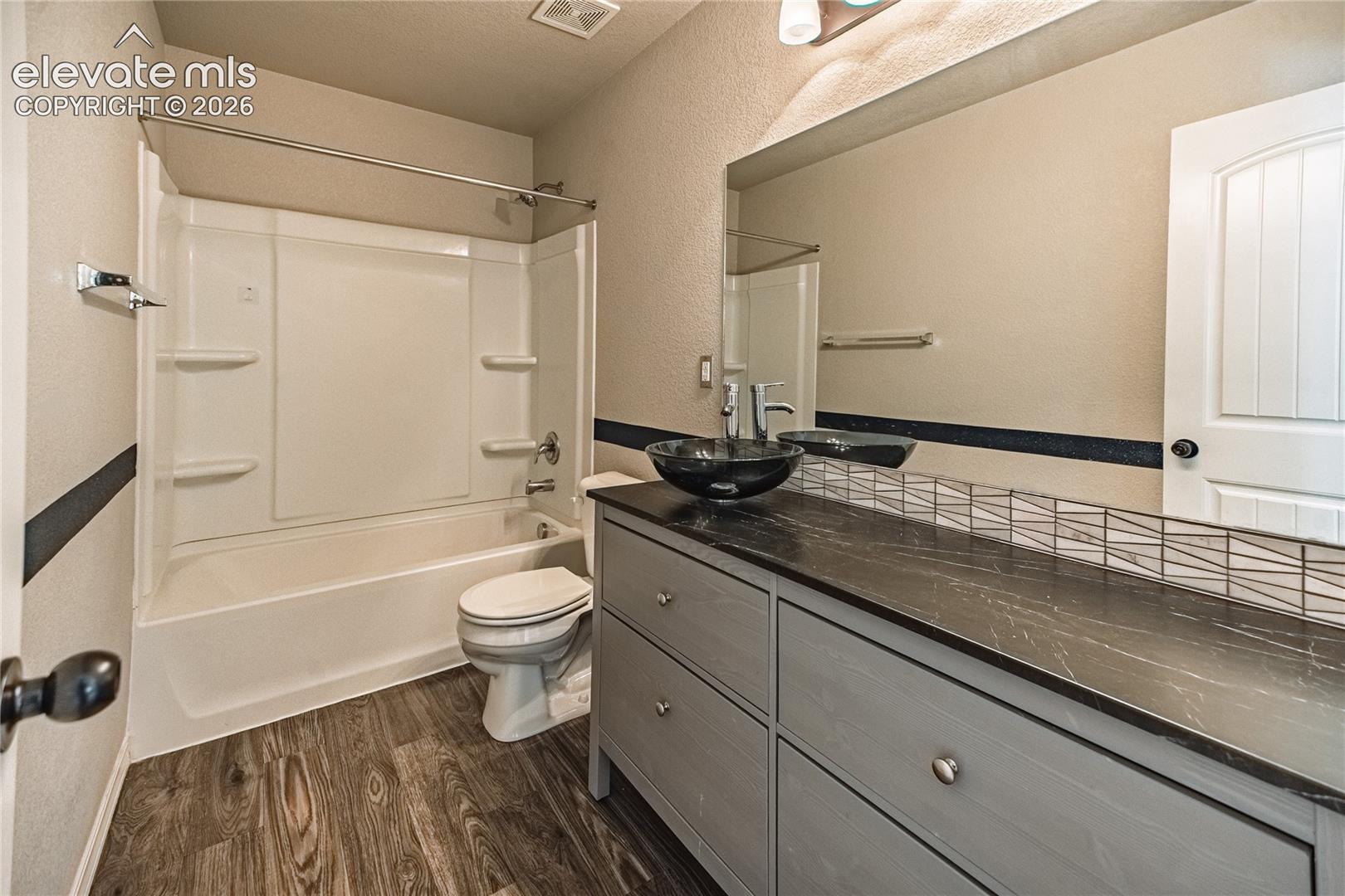 Wood-finish flooring, full bathtub/shower combination, dark stone-finish countertop, vessel sink, and an arched panel interior door