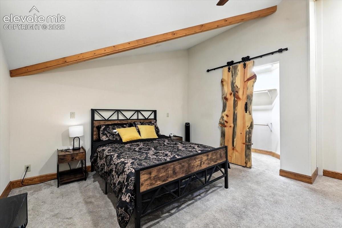 Vaulted ceiling featuring exposed wood beam accents, natural-edge wood sliding barn door, and carpeted flooring