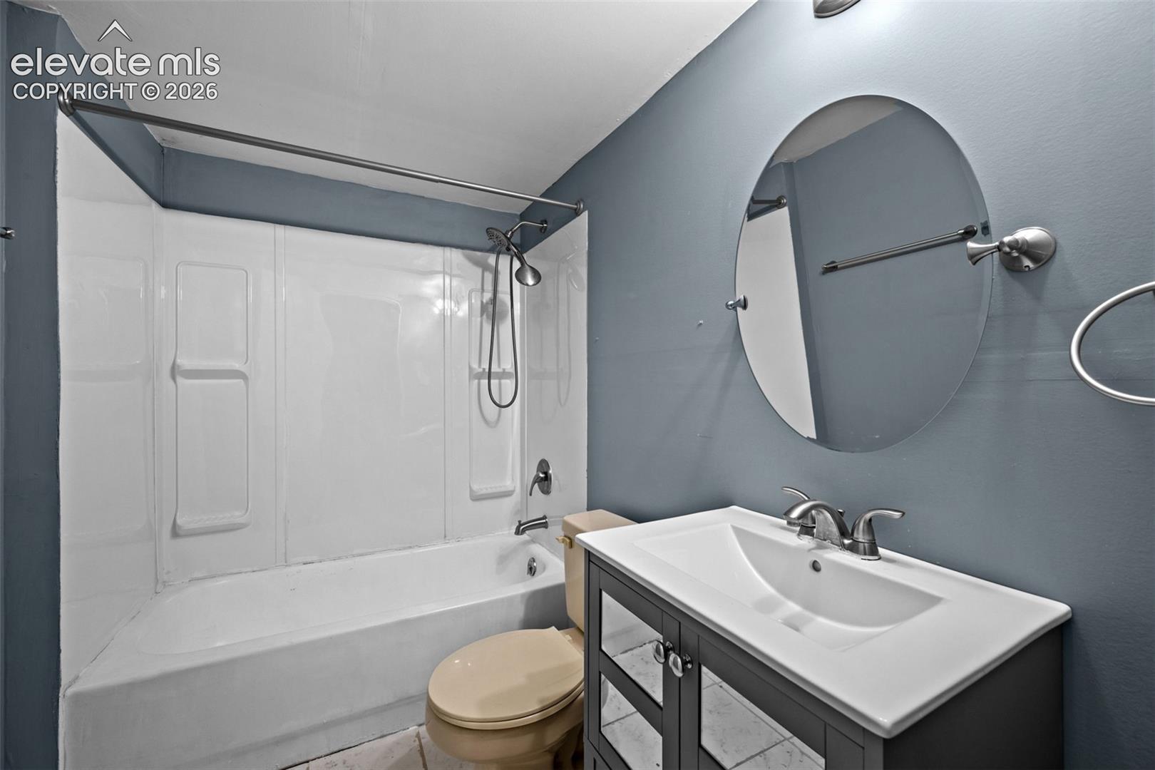 Bathroom featuring a bathtub and shower combination with white surround, oval wall-mounted mirror, and vanity with an integrated sink and chrome hardware