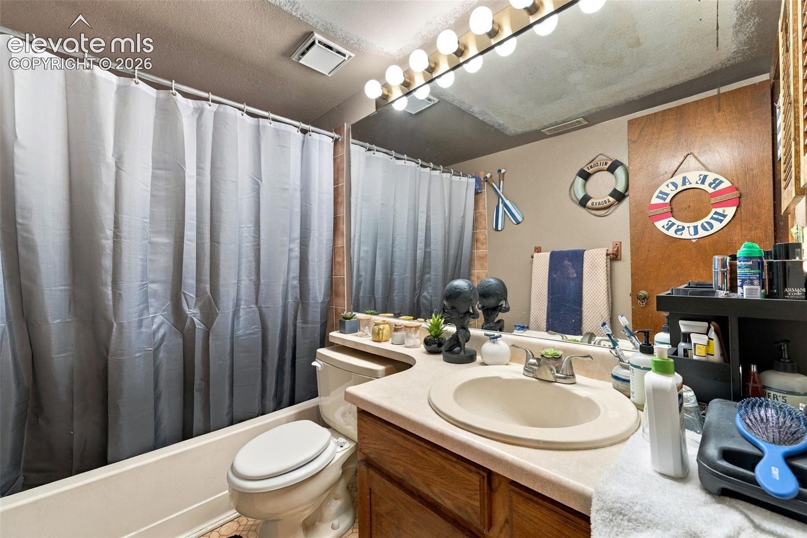 Bathroom featuring a single-sink vanity with a molded countertop, wood-finish cabinetry, full-width wall mirror, and a combination tub and shower