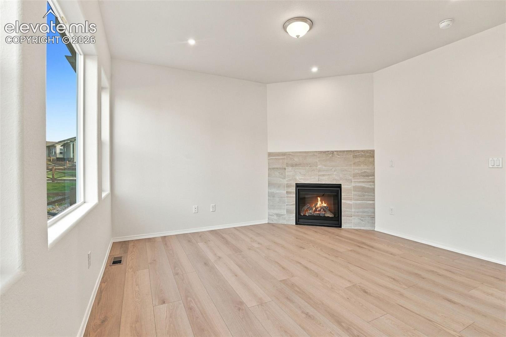 Corner fireplace featuring a linear stone-tile surround, light-toned wood-finish flooring, and large vertical windows