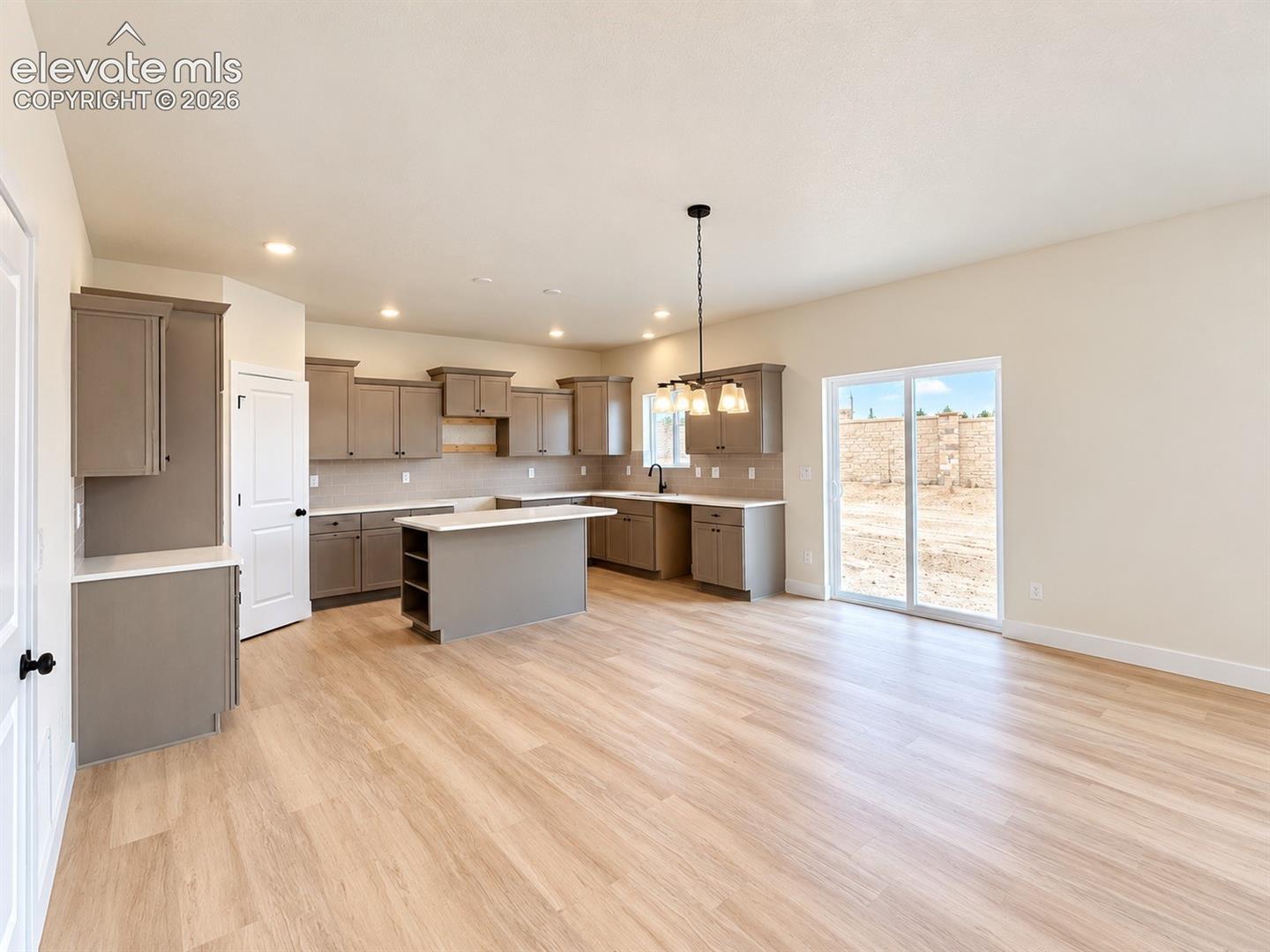 Open-concept kitchen featuring cabinetry in a neutral finish, a central island with a countertop, wood-finish flooring, recessed lighting, and sliding glass doors
