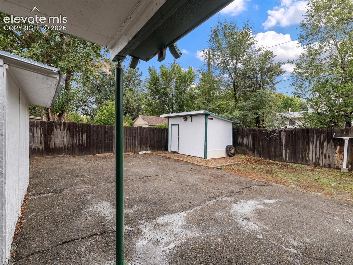 Private backyard with a wood fence, detached white shed, and mature trees