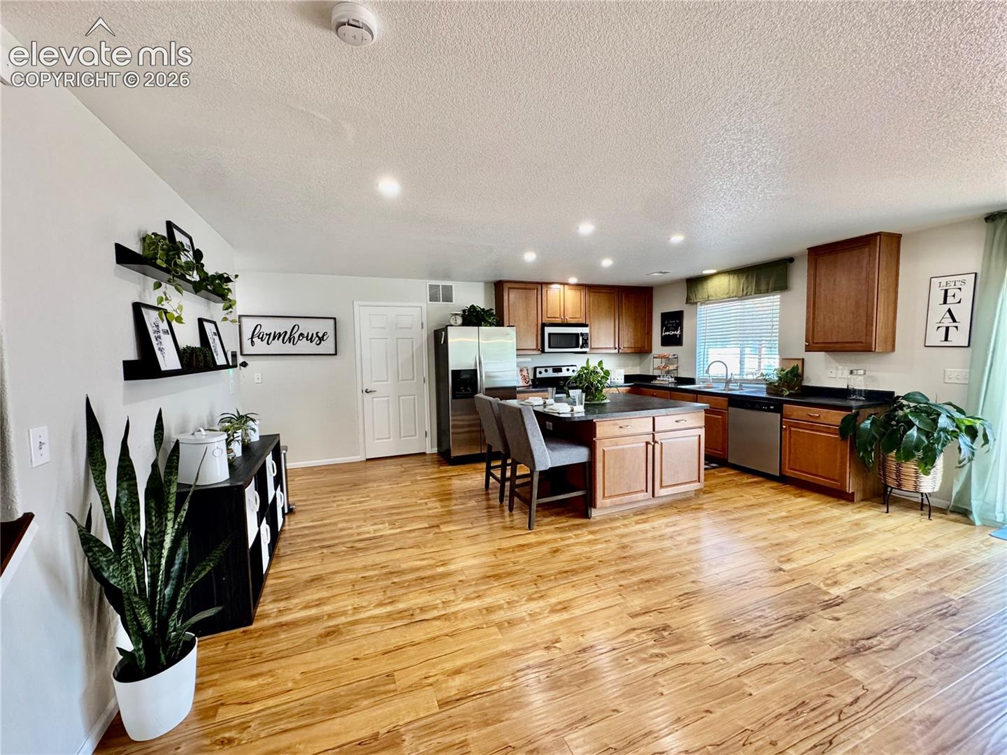 Open-concept kitchen featuring wood-finish flooring, recessed lighting, wood cabinetry, stainless steel appliances, and a central island with seating