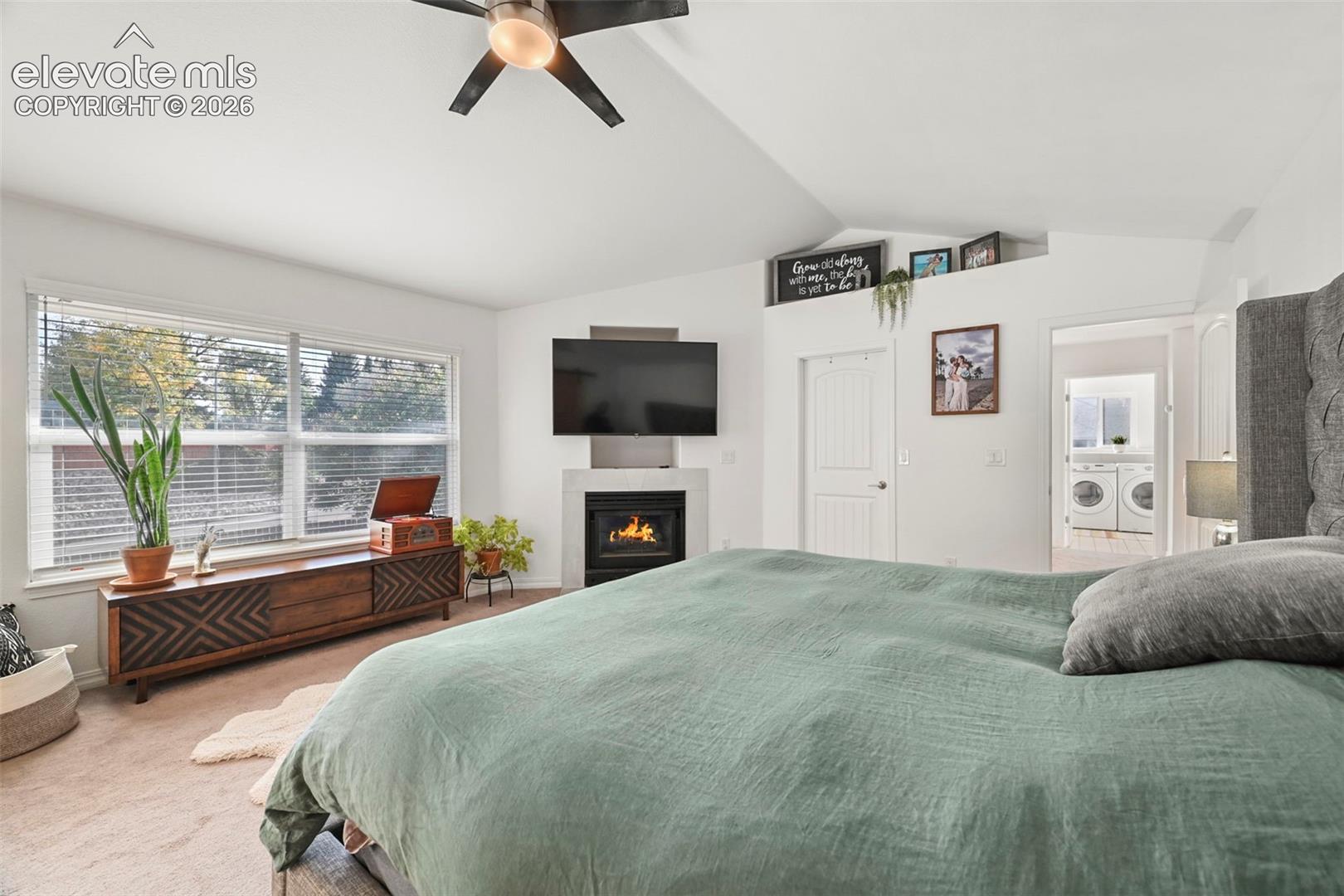 Vaulted ceiling with a ceiling fan, a prominent window with blinds, a wall-mounted television, and a built-in fireplace