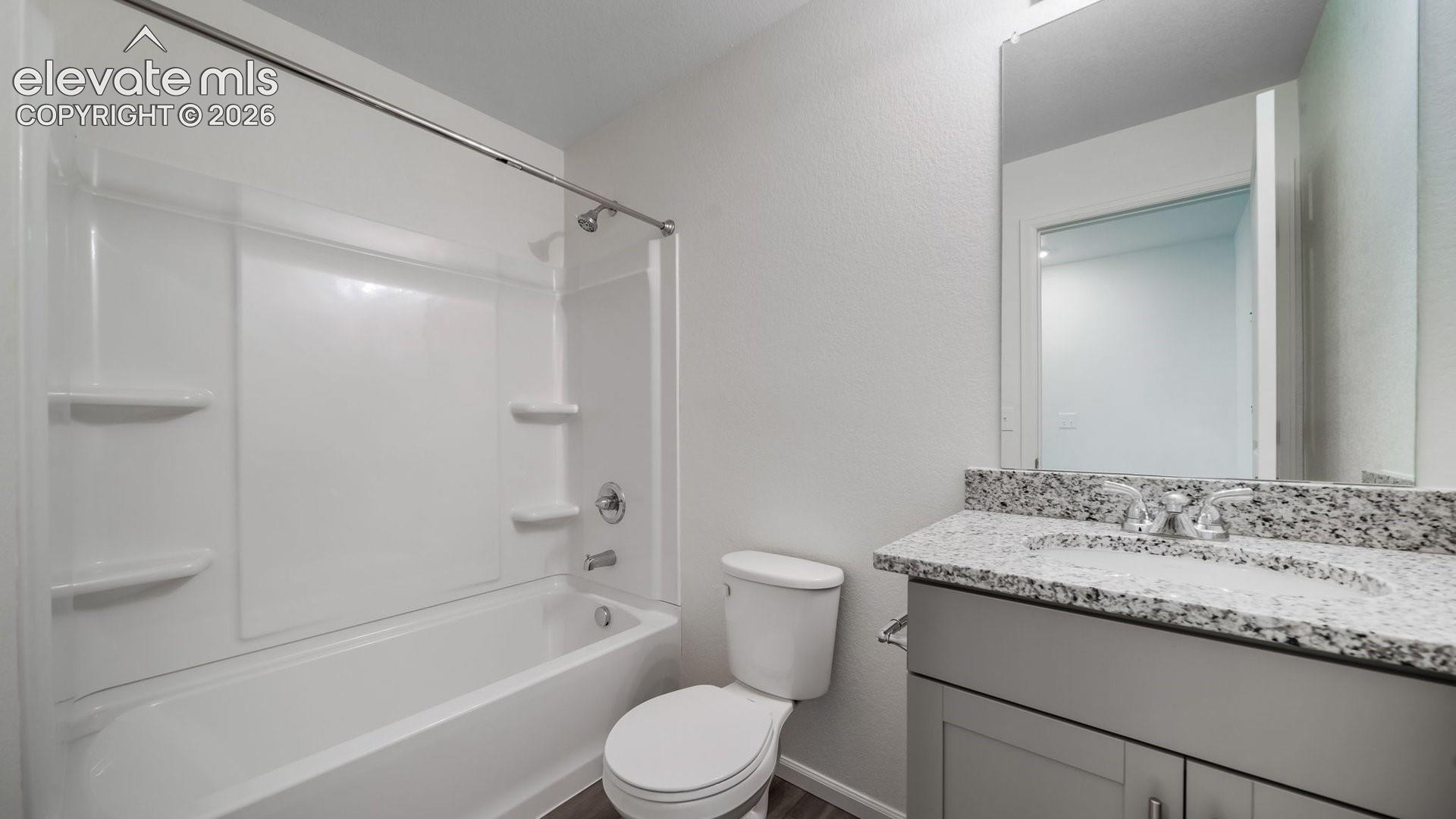 Bathroom featuring a vanity with a light-toned stone-finish countertop, a drop-in sink with chrome fixtures, a full-width mirror, and a shower-tub combination with built-in shelving
*photos of a model home*