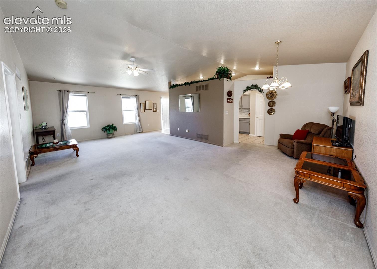 Expansive interior featuring high ceilings with a recessed light fixture, a prominent arched architectural opening, wall-to-wall carpeting, and multiple windows