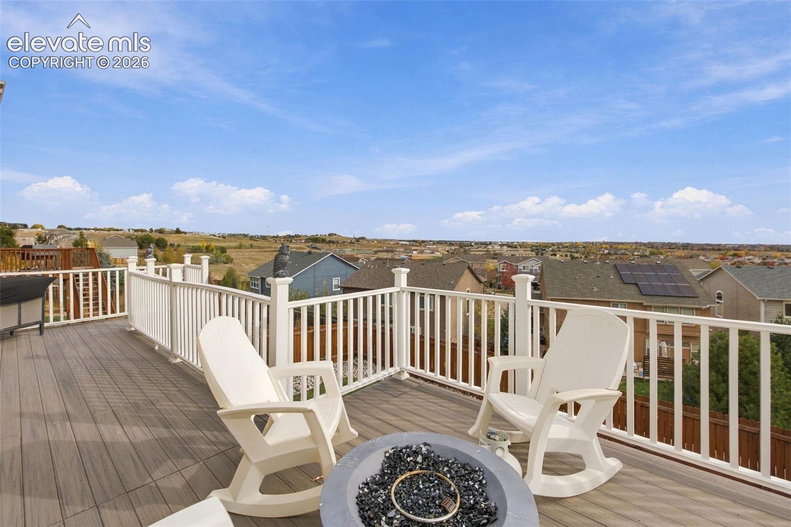 Elevated deck featuring composite decking, white vertical baluster railing, and a circular fire pit