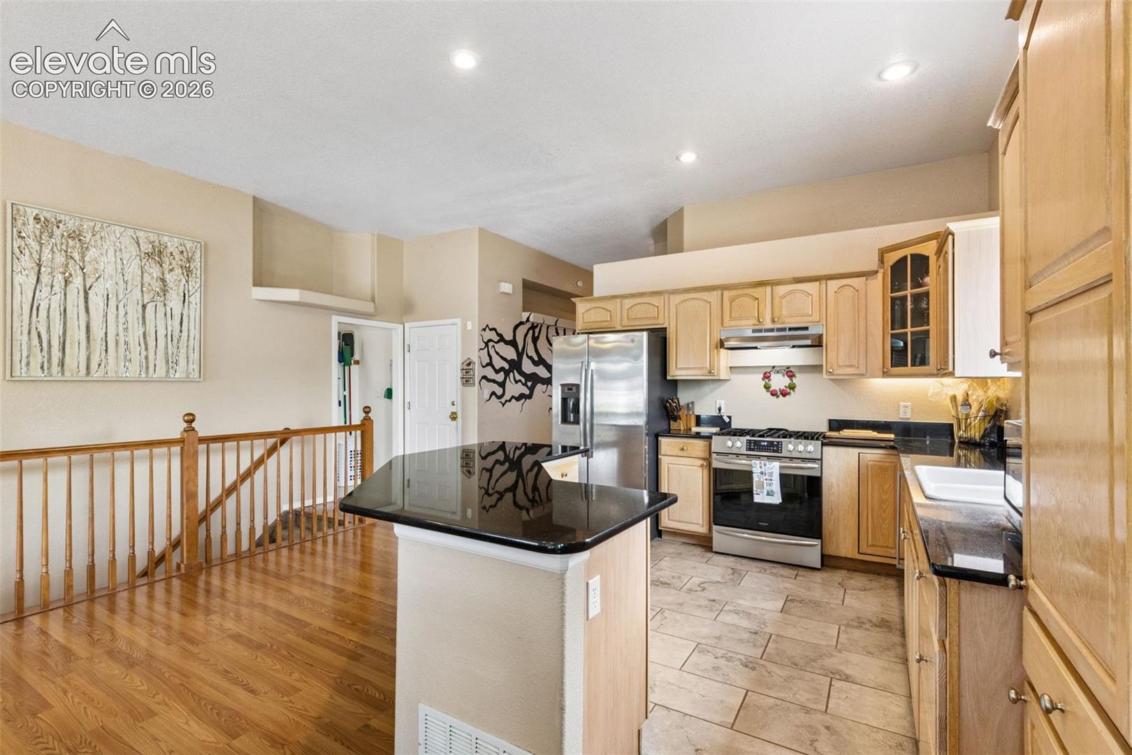 Kitchen featuring light wood cabinetry, stone countertops, stainless steel appliances, tile flooring, and a breakfast bar
