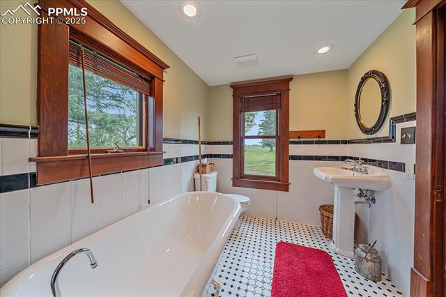 Full bath with tile walls, a freestanding tub, a wainscoted wall, and recessed lighting