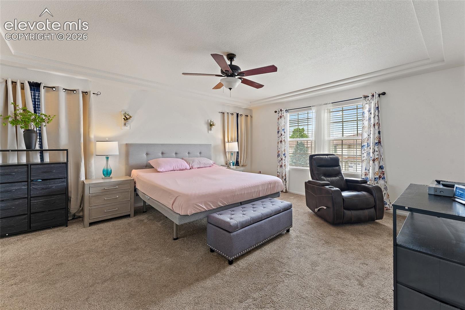 Room featuring tray ceilings, neutral carpeting, a central ceiling fan with integrated lighting, and dual wall-mounted light fixtures