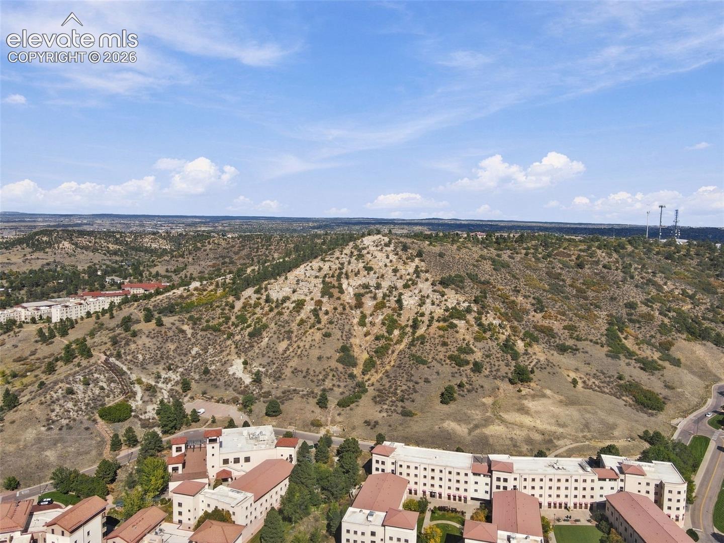 Aerial perspective of a multi-building property complex featuring light-toned masonry facades, clay tile roofing, and an elevated hillside backdrop