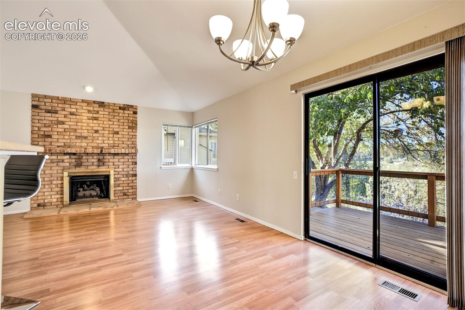 Floor-to-ceiling brick fireplace with a stone hearth, wood-finish flooring, multi-globe chandelier, and sliding glass doors opening to an exterior deck