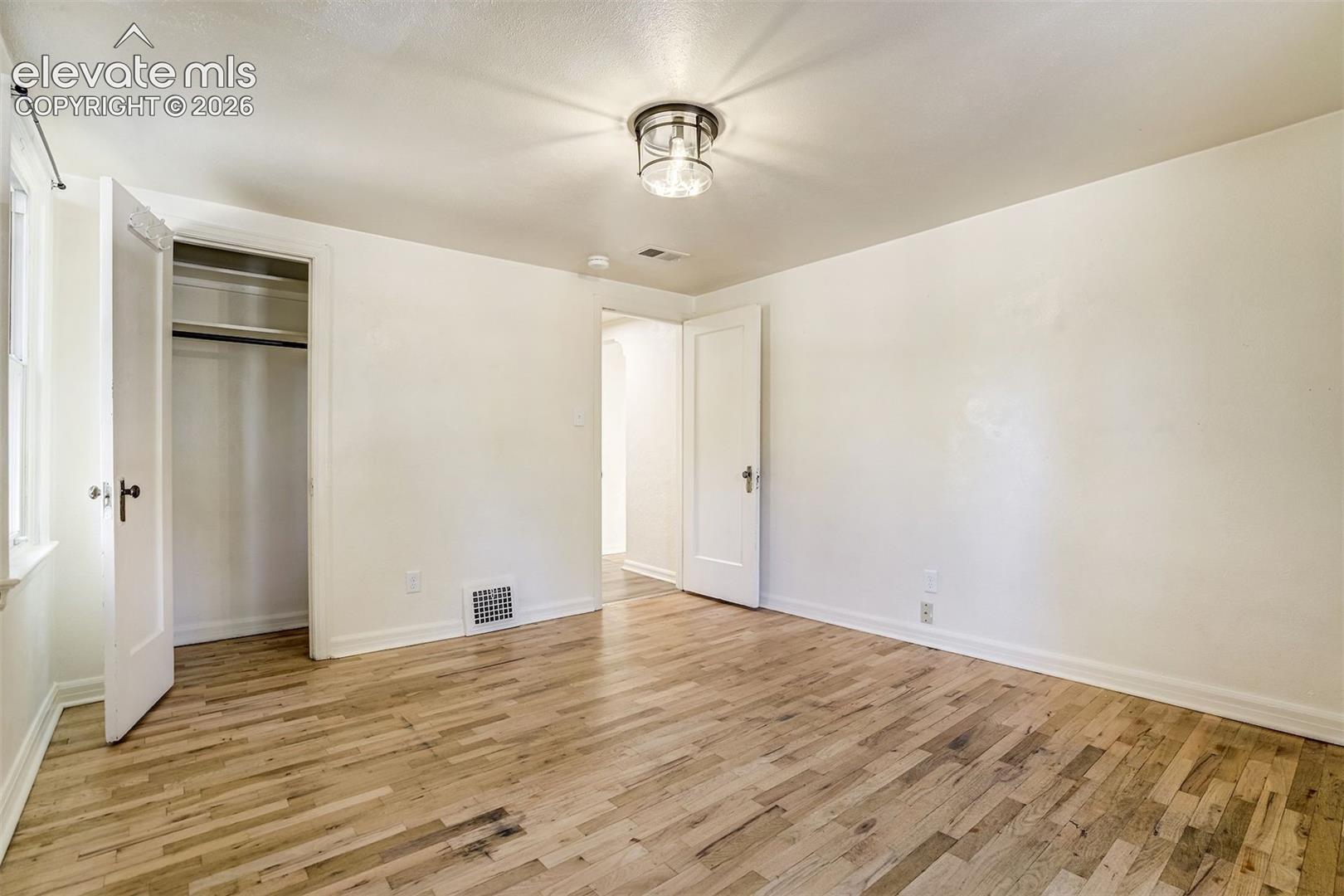 Room featuring wood-finish flooring, a flush-mount drum-style light fixture, a closet with a single hanging rod, and solid-core interior doors