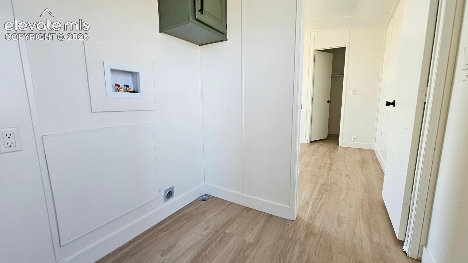 Utility space featuring wood-finish flooring, a wall-mounted sage green cabinet, and dedicated hookups for laundry appliances