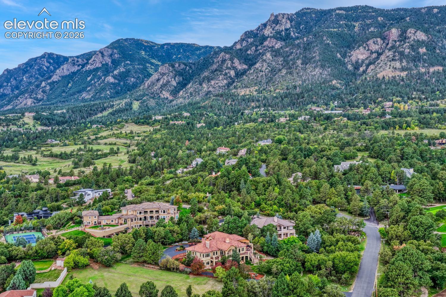 Aerial perspective of a sprawling hillside estate featuring mature evergreen landscaping, multi-level structures with clay tile roofing, and expansive mountain backdrops