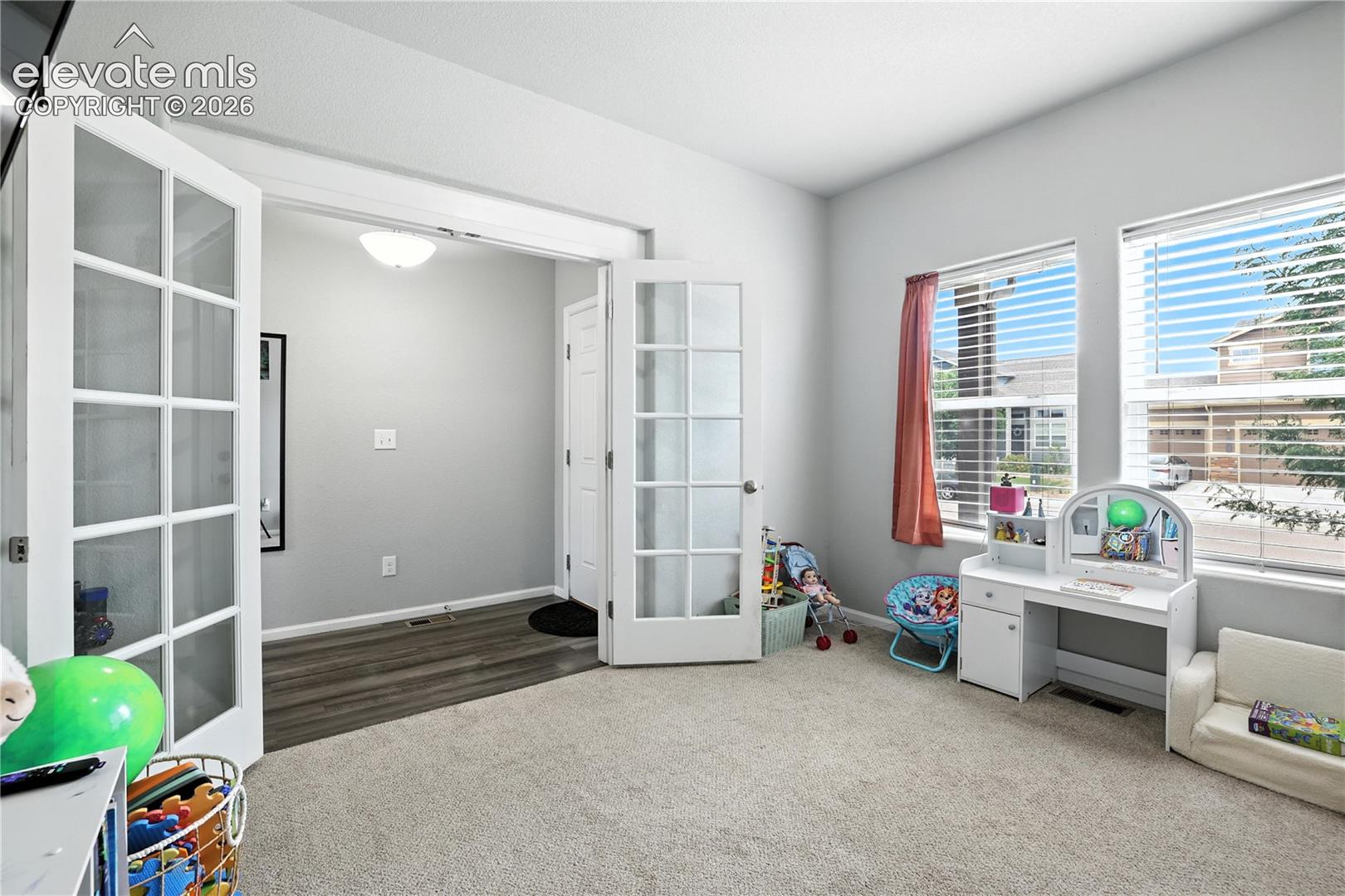 French doors with glass panels, light carpet flooring, large windows with blinds, and a built-in overhead light fixture