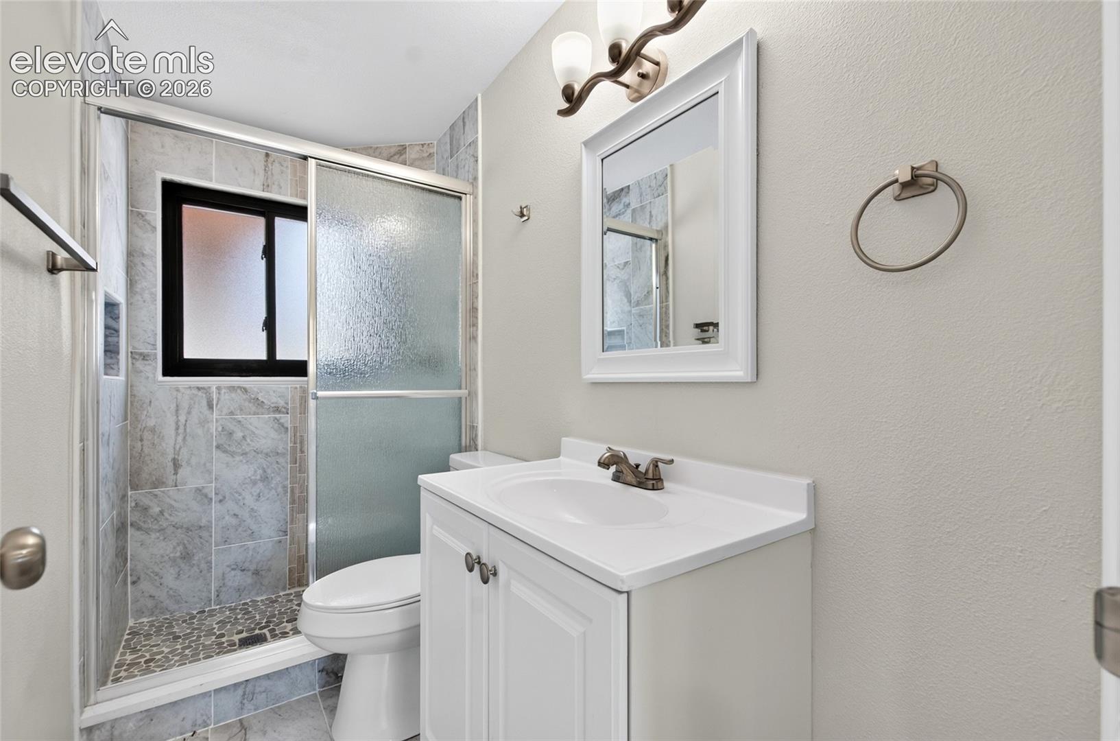 Bathroom featuring a tiled shower with a sliding glass door, pebble floor, and integrated window