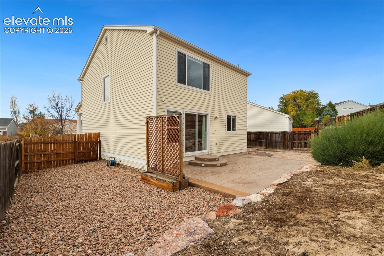 Exterior featuring light-toned horizontal siding, a stamped concrete patio, a decorative lattice privacy screen, and fenced perimeter