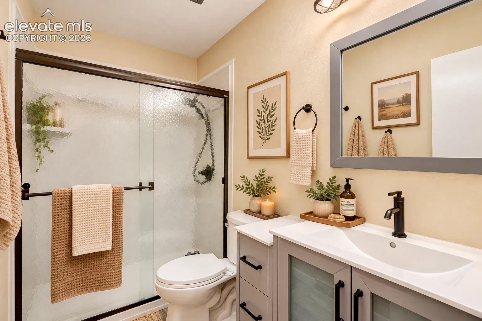Bathroom featuring a grey vanity with a white integrated sink, matte black faucet, framed mirror, and a walk-in shower with textured glass sliding doors. AI-Enhanced – furniture/decor digitally added