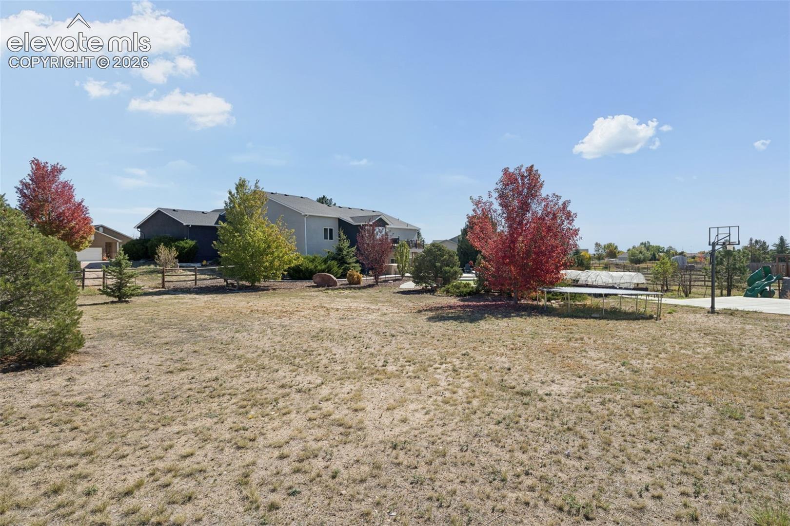 Expansive yard featuring a basketball court, mature trees, and a wooden perimeter fence
