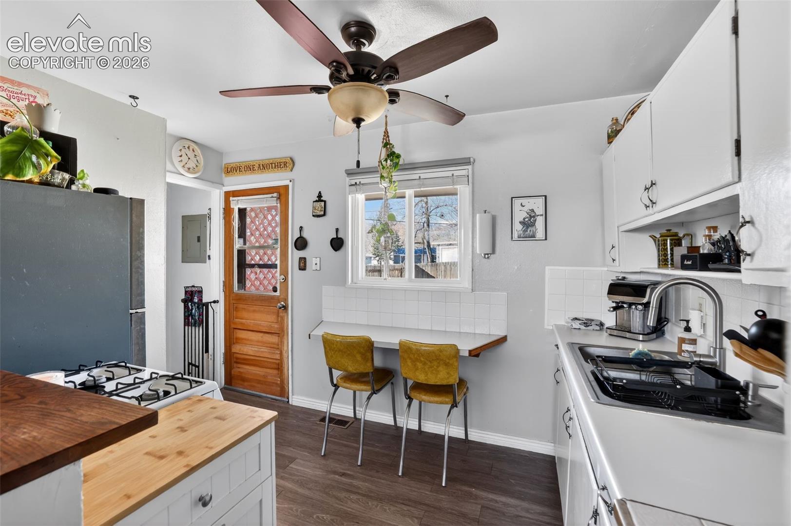 Well-lit kitchen featuring white cabinetry, a built-in folding counter, wood-finish flooring, and a ceiling fan