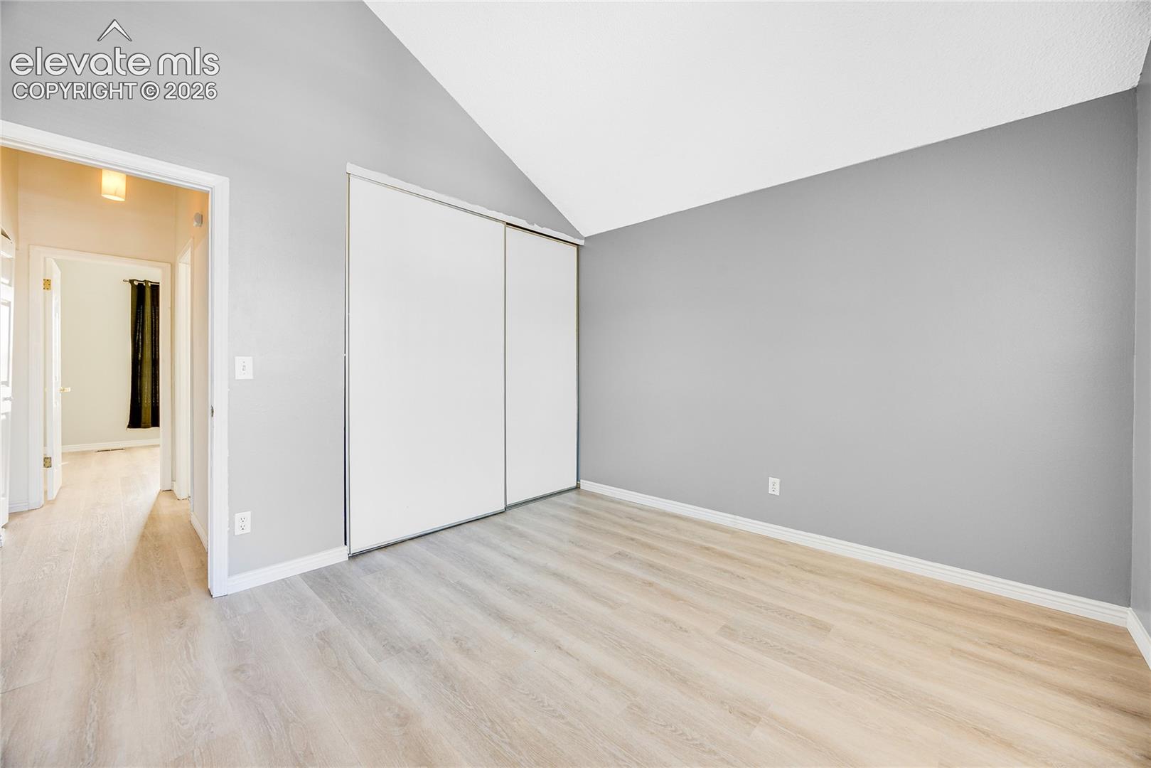 Vaulted ceiling, wood-finish flooring, sliding closet doors, and light gray wall paint