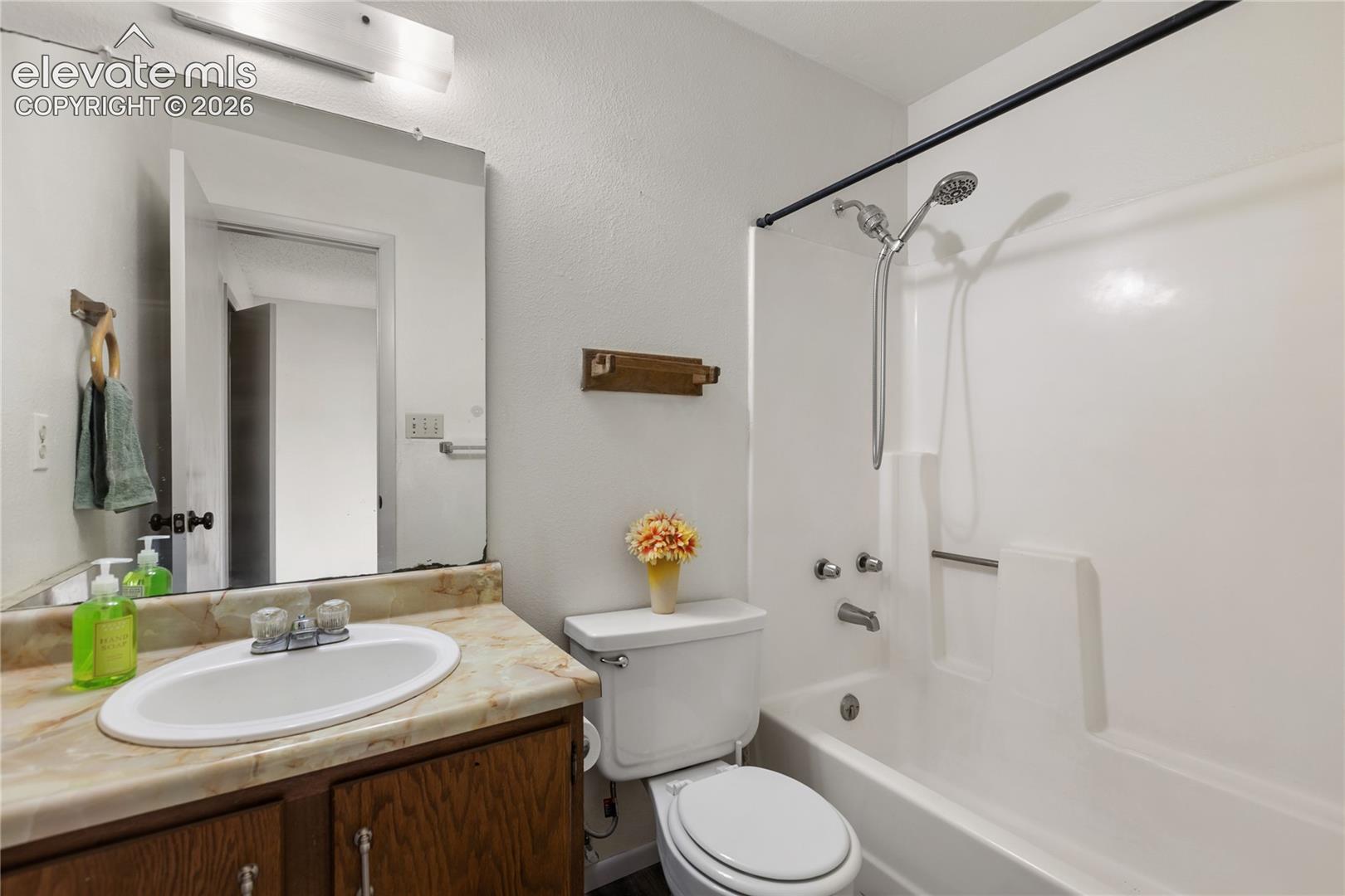 Bathroom featuring a white tub/shower combination with a handheld showerhead, a toilet, a vanity with a white oval sink, and a countertop with a stone-finish
