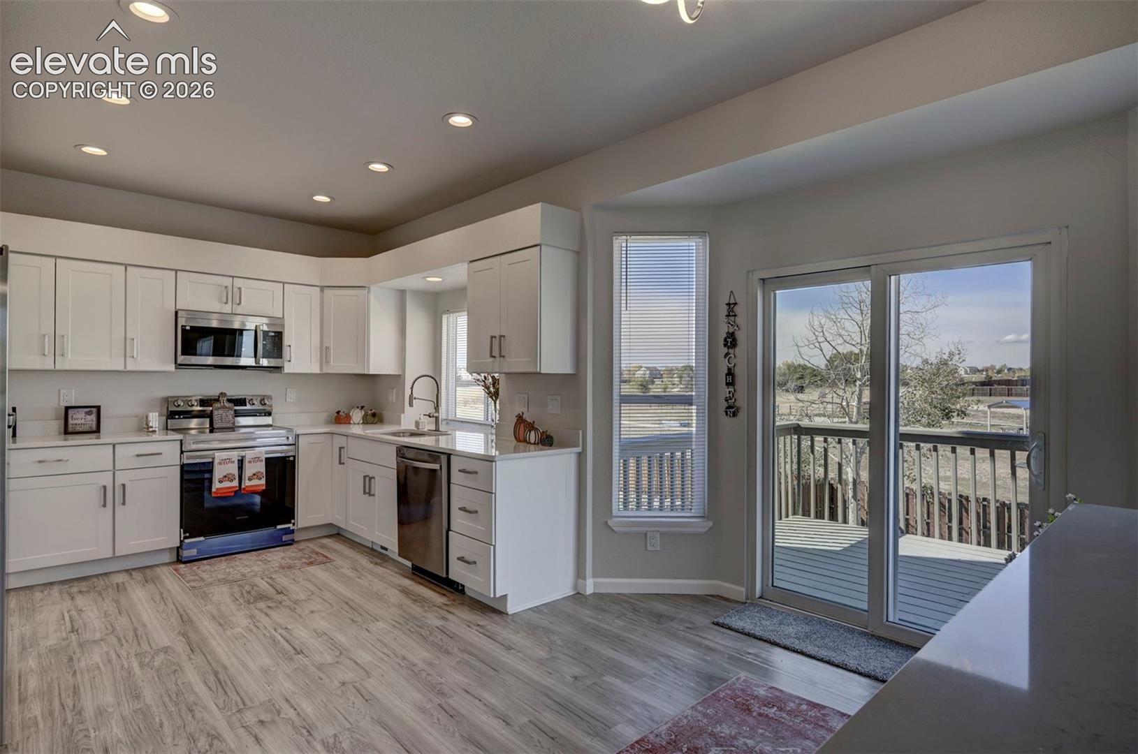 Kitchen featuring white cabinetry, stainless steel appliances, wood-finish flooring, recessed lighting, and a sliding glass door providing external access