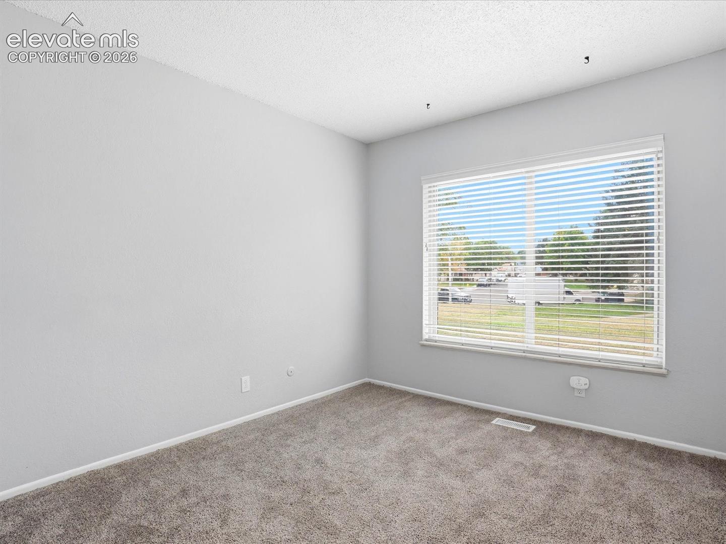 Neutral wall tones, wall-to-wall carpeting, and a large window featuring horizontal blinds