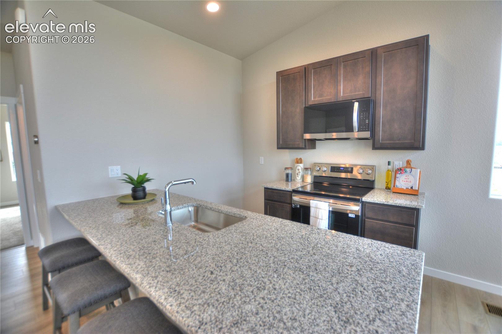 Granite-style countertop with an undermount sink, stainless steel faucet, dark wood-finish cabinetry, and stainless steel appliances