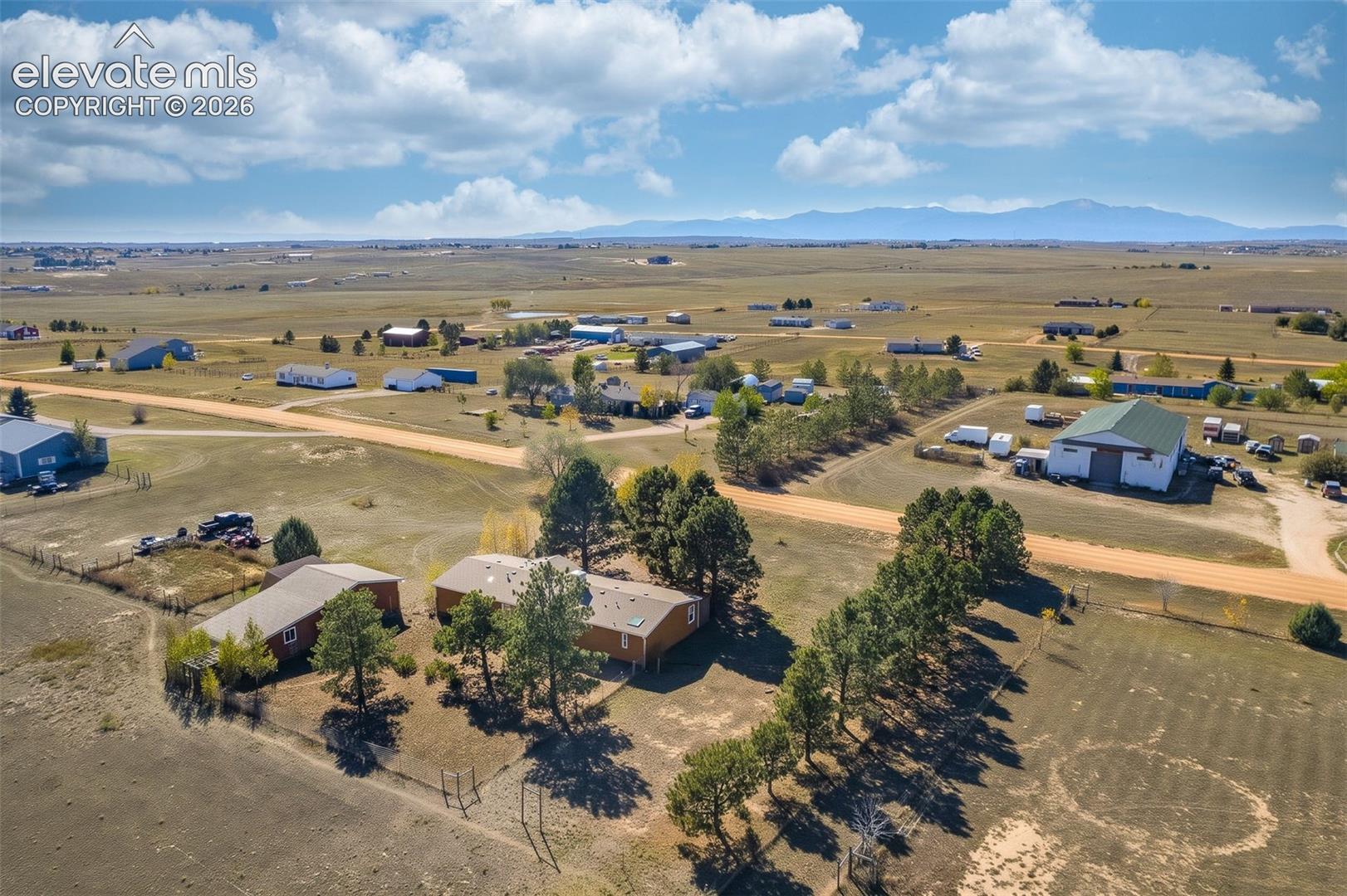 Aerial perspective of a multi-structure property featuring mature evergreen trees, expansive acreage, and a distant mountain backdrop