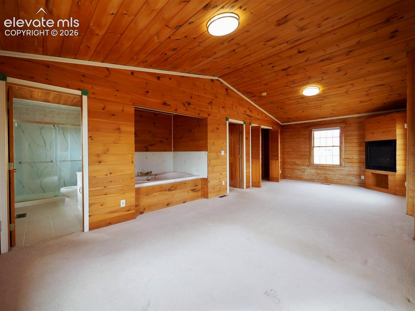 Vaulted ceilings with natural wood-plank walls and ceiling, recessed jetted tub, built-in fireplace, and attached bathroom with glass-enclosed shower