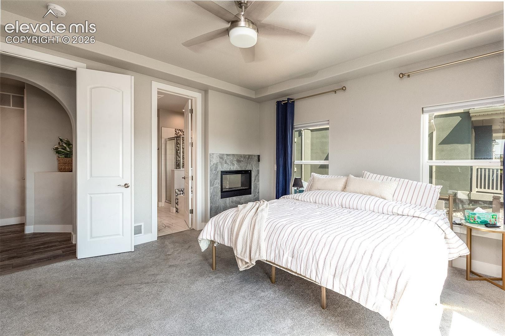 Dual sided gas fireplace with stone surround, ceiling fan, arched doorway, and light carpeting