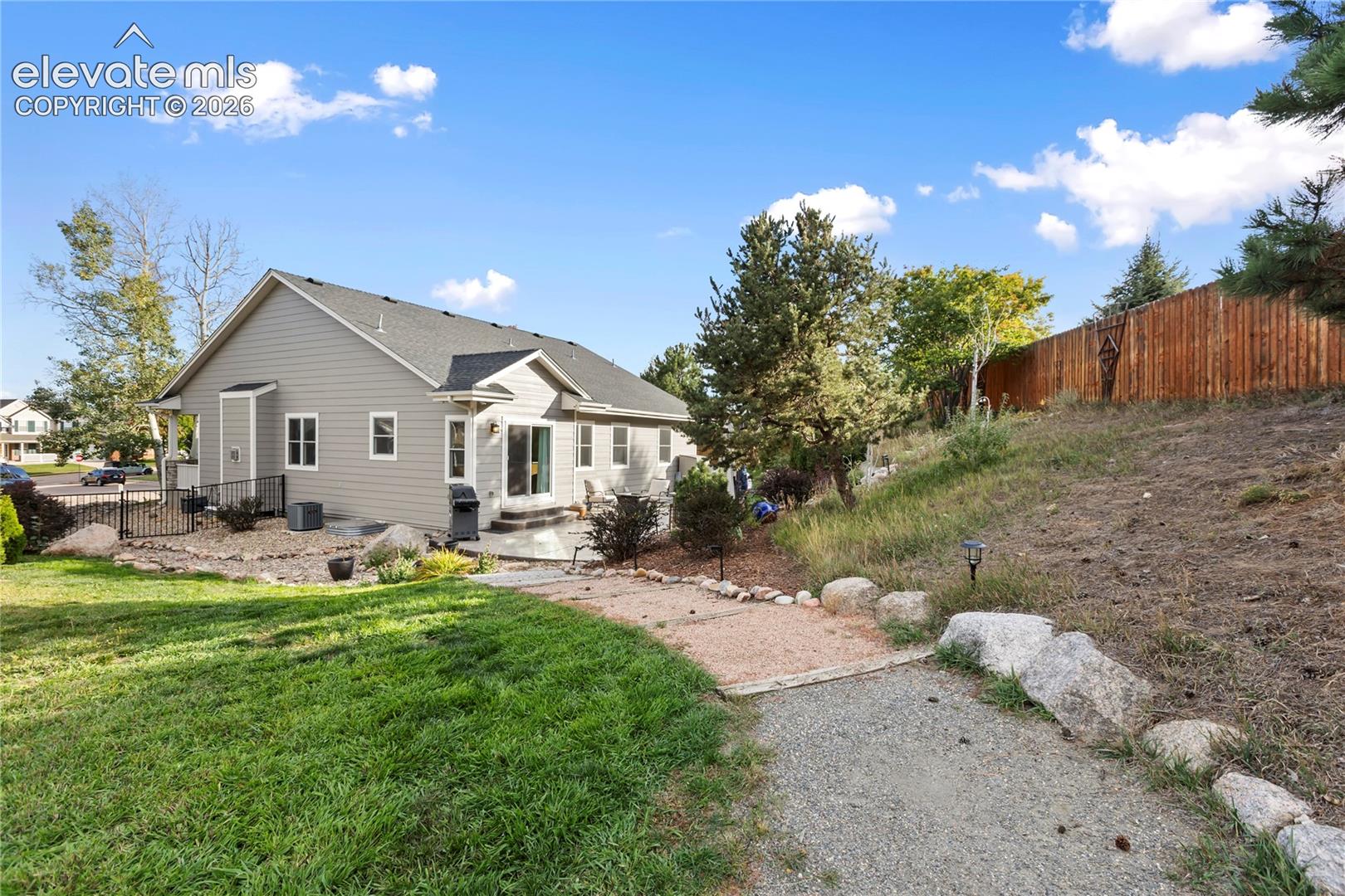 Gray siding exterior with multiple windows, a rear patio, and a gravel pathway