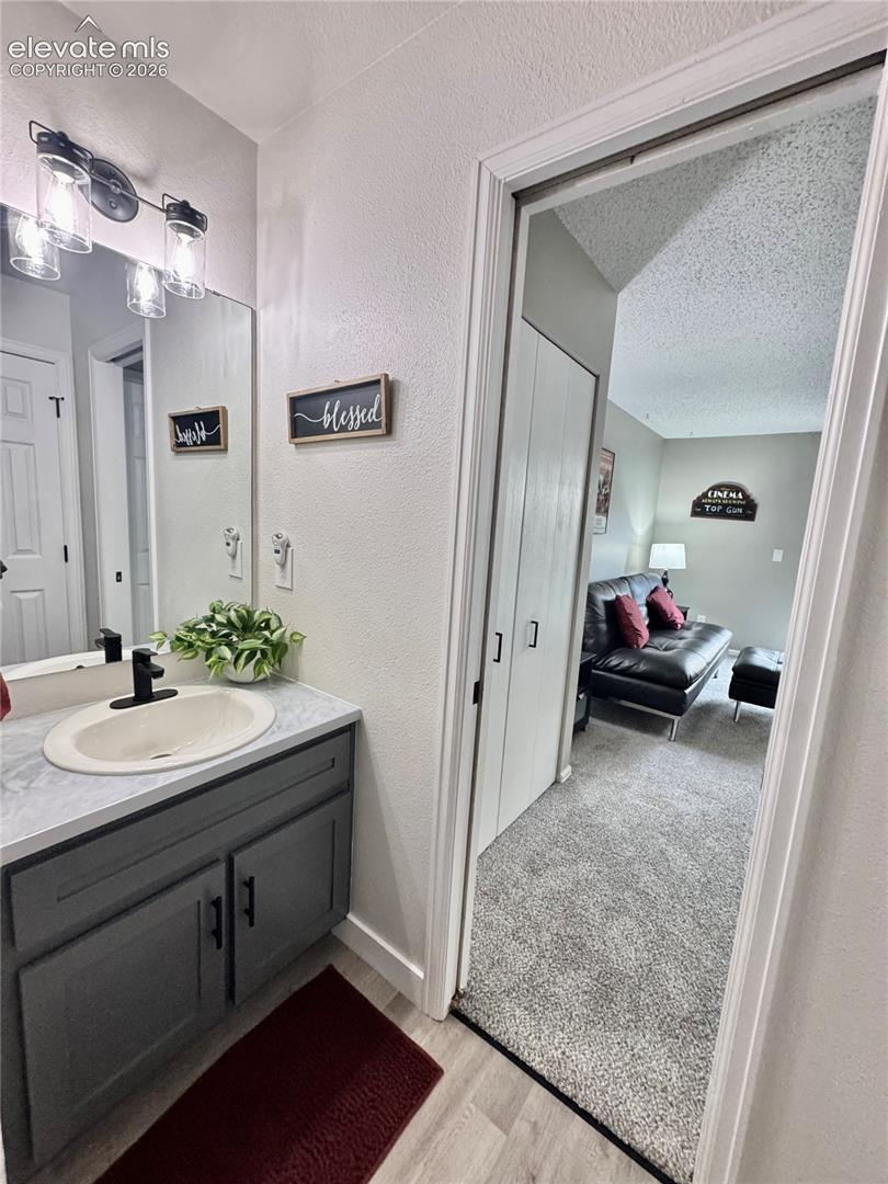 Bathroom vanity featuring dark gray cabinetry, stone-finish countertop, oval undermount sink, matte black faucet, and three-light wall fixture above a large mirror