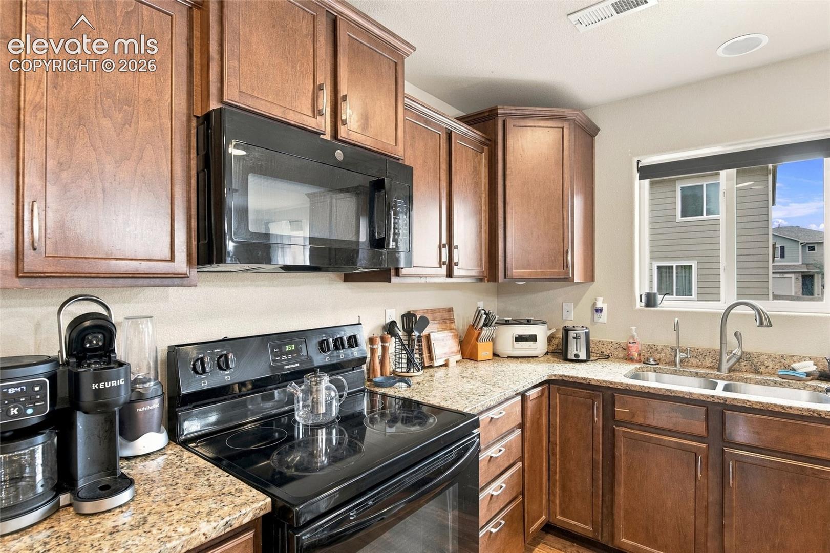 Kitchen featuring wood cabinetry, stone countertops, dual-basin stainless steel sink with pull-down faucet, and built-in black microwave and range