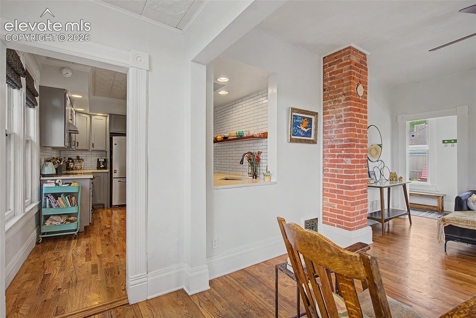 Living area featuring hardwood flooring, exposed brick, natural lighting and entrance to the updated kitchen